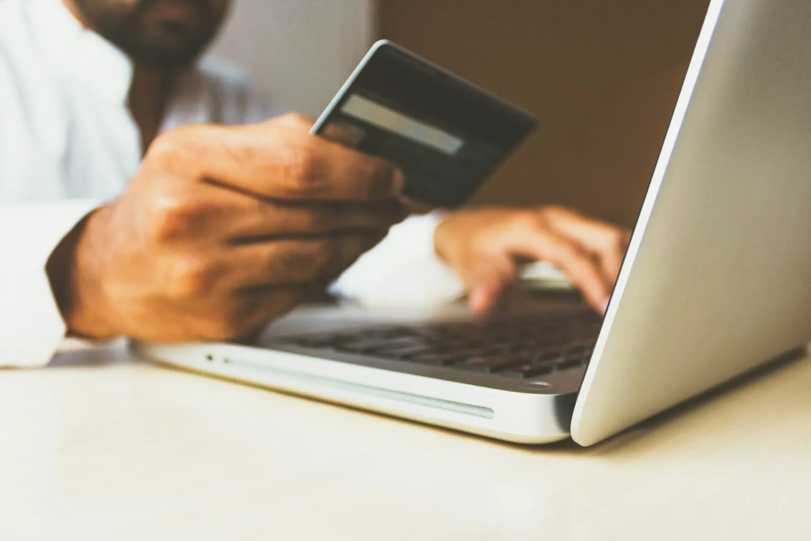 A hand holding a credit card next to a laptop, paying online